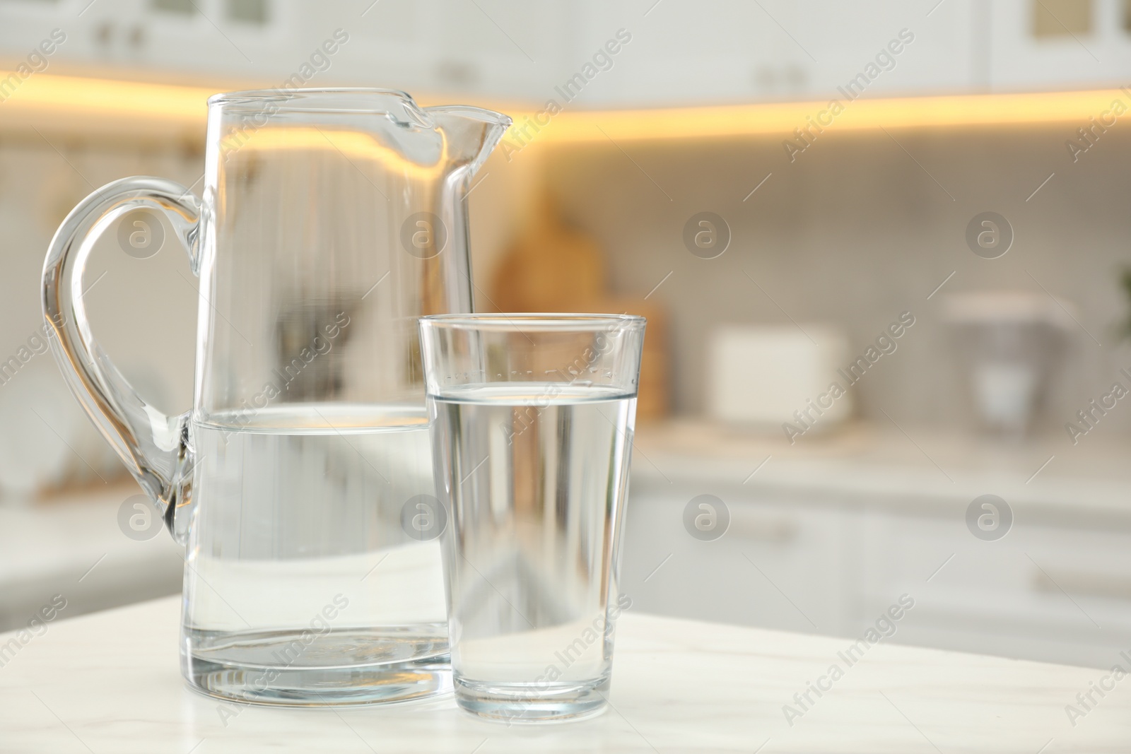 Photo of Jug and glass with clear water on white table in kitchen, space for text