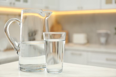 Jug and glass with clear water on white table in kitchen, space for text