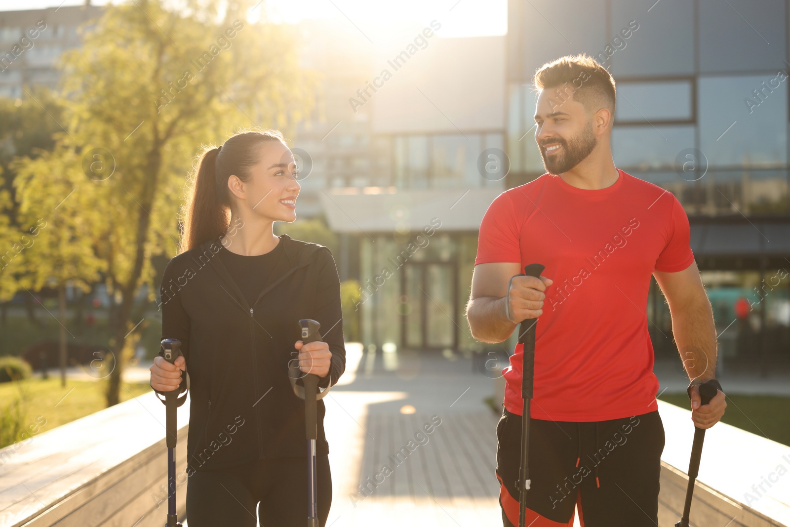 Photo of Happy couple practicing Nordic walking with poles outdoors on sunny day