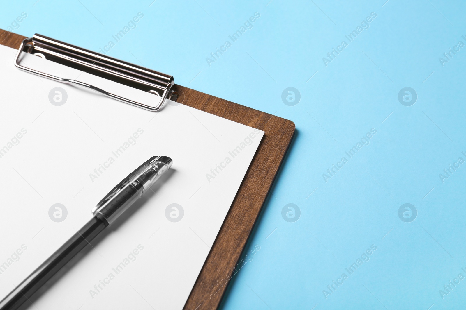 Photo of New wooden clipboard with sheet of blank paper and pen on light blue background. Space for text