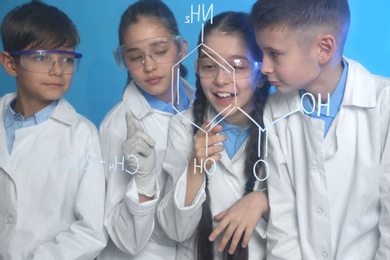 Pupils studying chemistry formula on glass board against color background