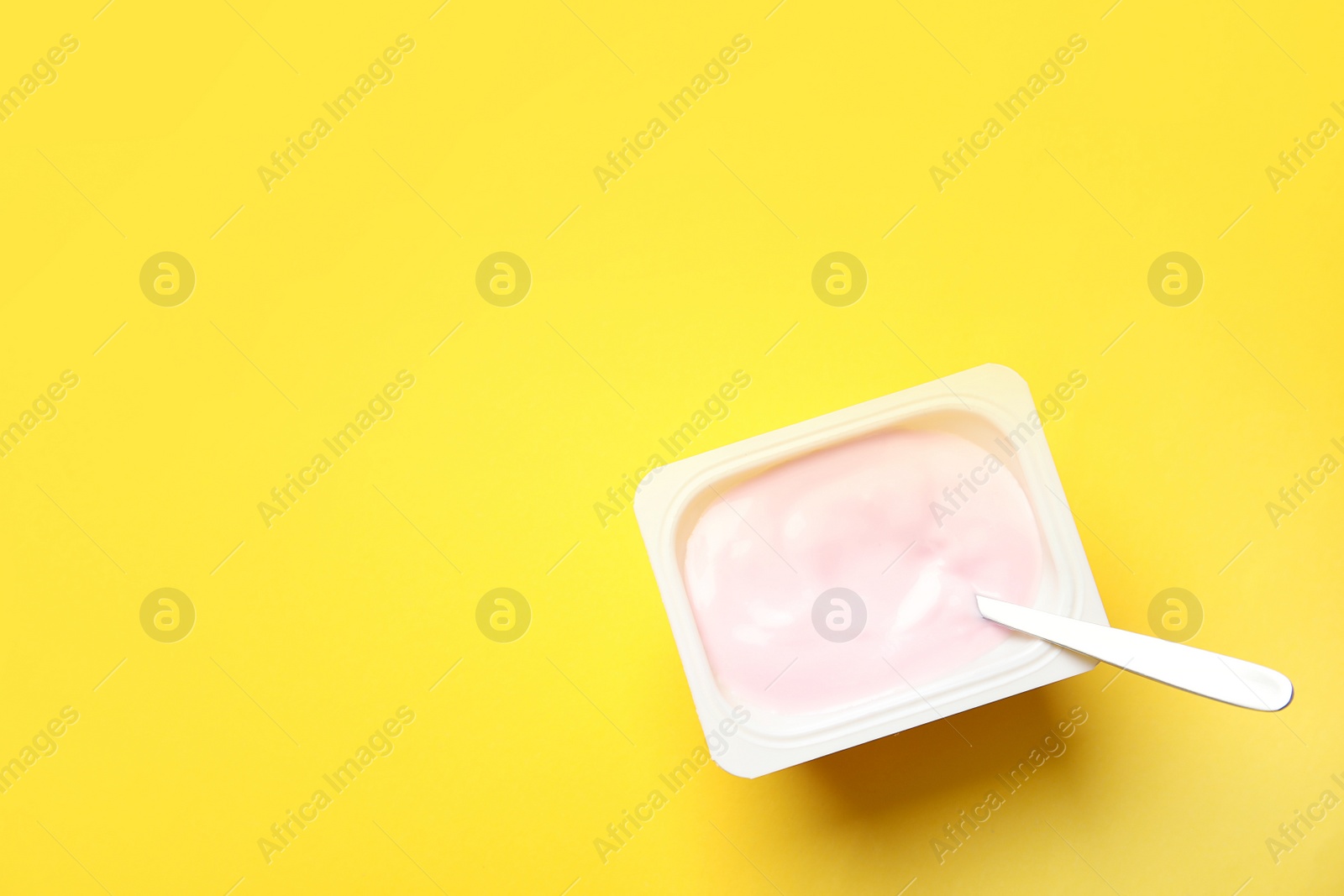 Photo of Plastic cup with creamy yogurt and spoon on color background, top view. Space for text