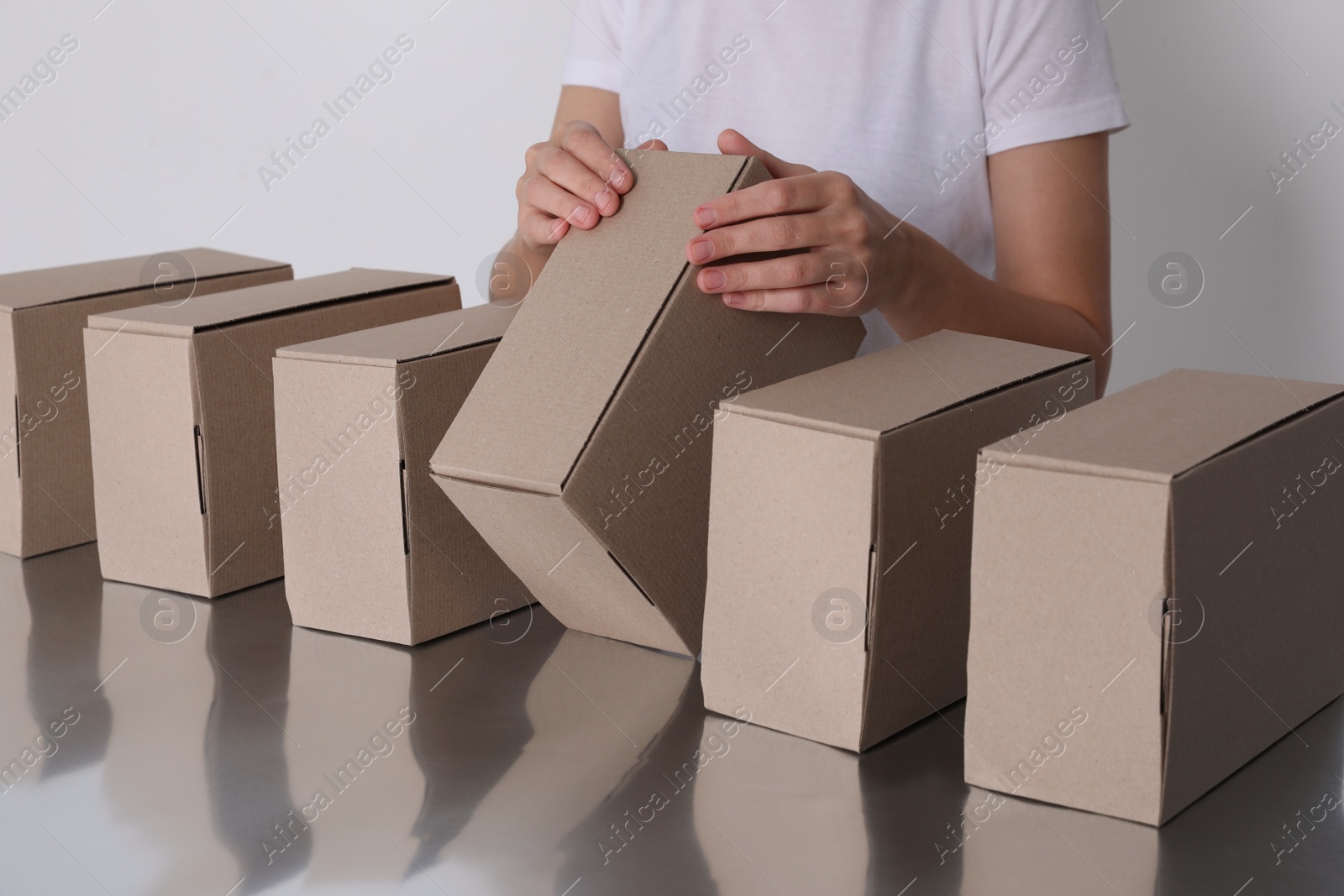 Photo of Woman folding cardboard boxes at table, closeup. Production line