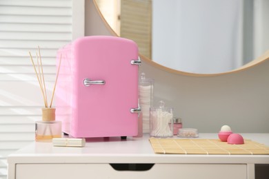 Photo of Cosmetics refrigerator and skin care products on white vanity table indoors