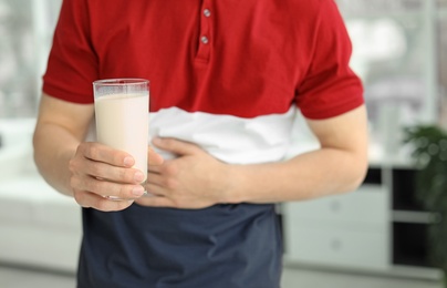Young man with dairy allergy holding glass of milk indoors