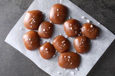 Photo of Tasty caramel candies and salt on grey table, top view