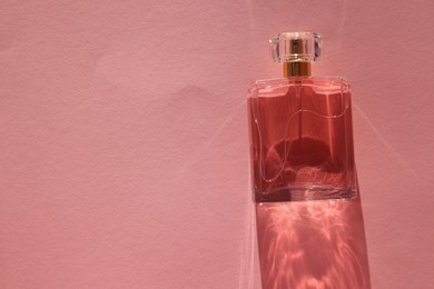 Luxury women's perfume. Sunlit glass bottle on pink background, top view. Space for text