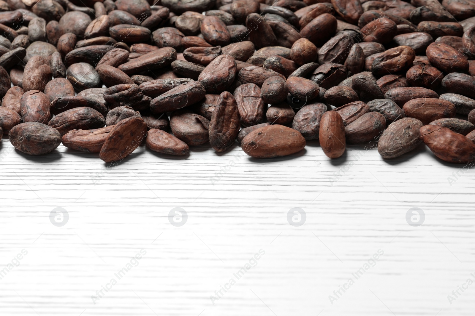 Photo of Tasty cocoa beans on white wooden table, space for text