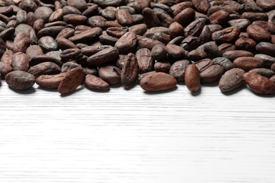 Photo of Tasty cocoa beans on white wooden table, space for text