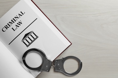 Photo of Criminal Law book and handcuffs on white wooden background, top view. Space for text