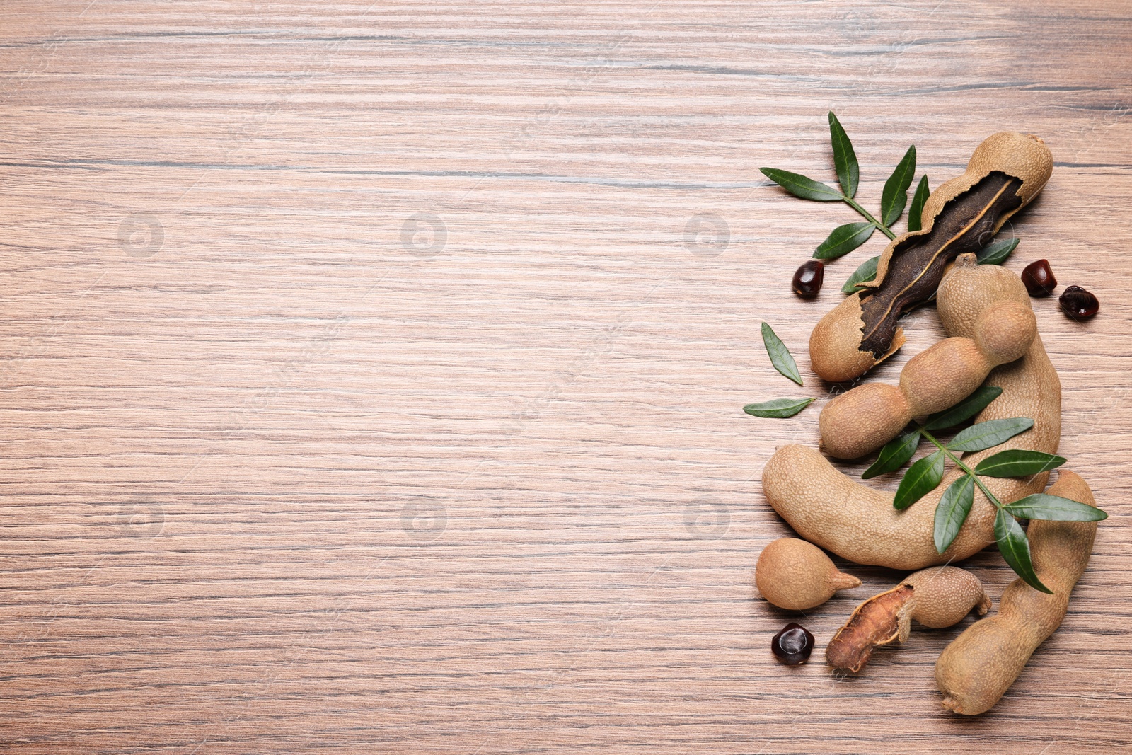 Photo of Delicious ripe tamarinds and leaves on wooden table, flat lay. Space for text