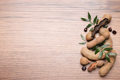 Photo of Delicious ripe tamarinds and leaves on wooden table, flat lay. Space for text