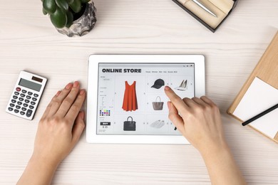 Photo of Woman with tablet shopping online at white wooden table, top view