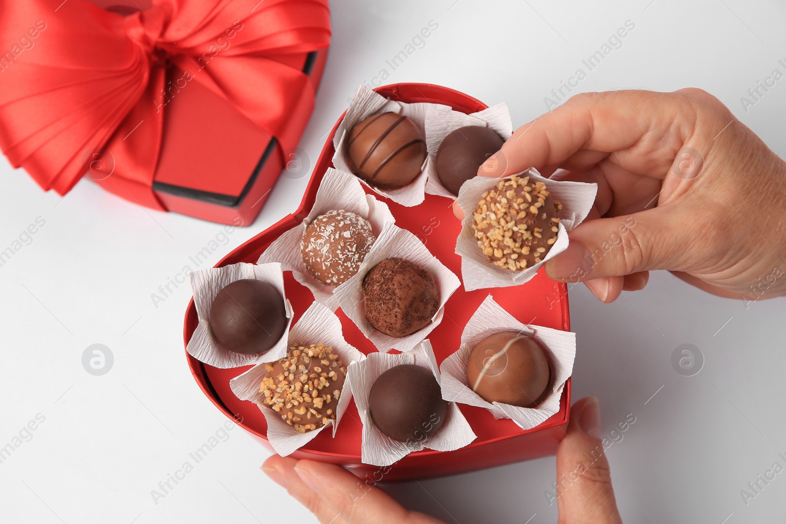 Photo of Woman taking delicious chocolate candy from heart shaped box on white background, above view