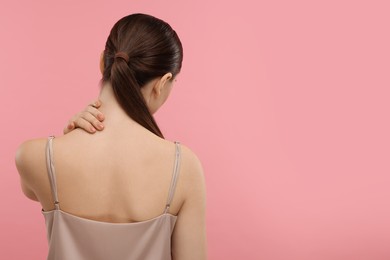 Photo of Woman touching her neck on pink background, back view. Space for text