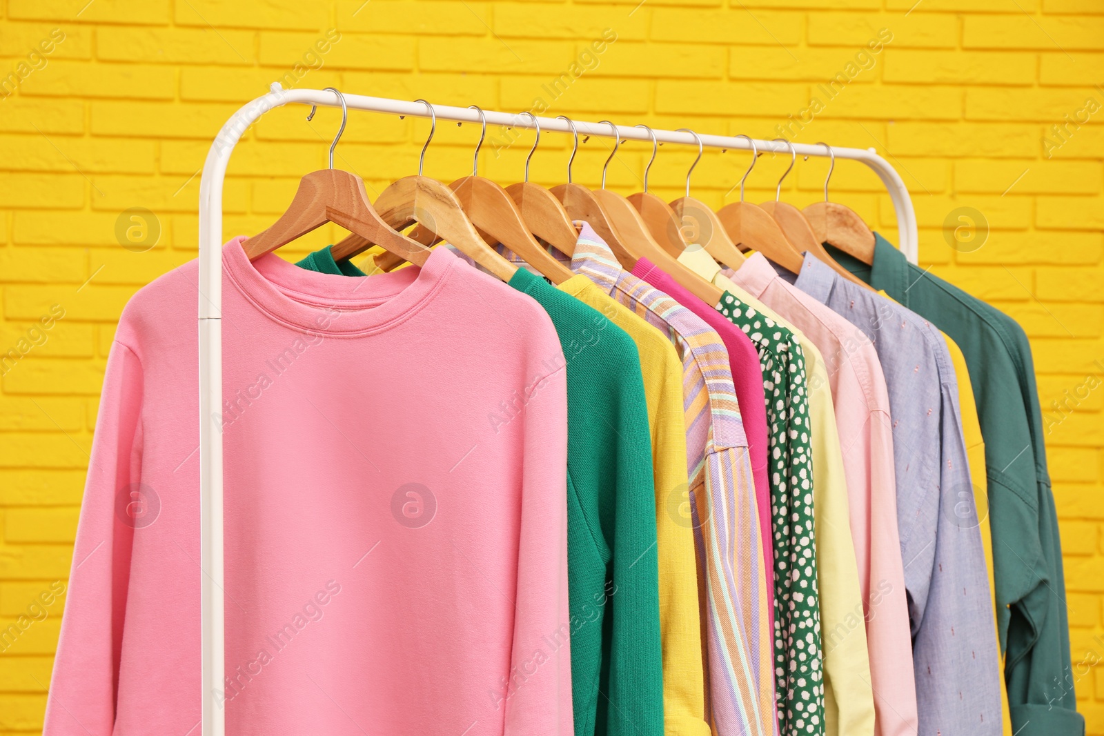 Photo of Rack with stylish clothes near yellow brick wall