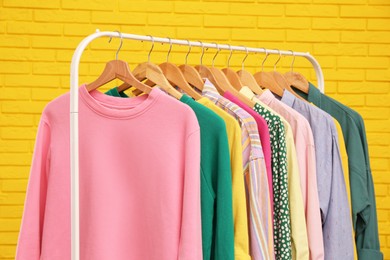 Photo of Rack with stylish clothes near yellow brick wall