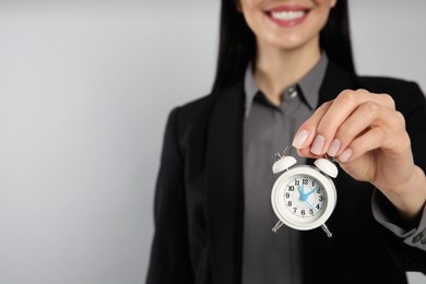 Photo of Businesswoman holding alarm clock on light grey background, closeup with space for text. Time management