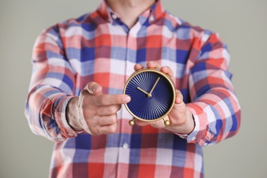 Photo of Young man holding alarm clock on grey background. Time concept