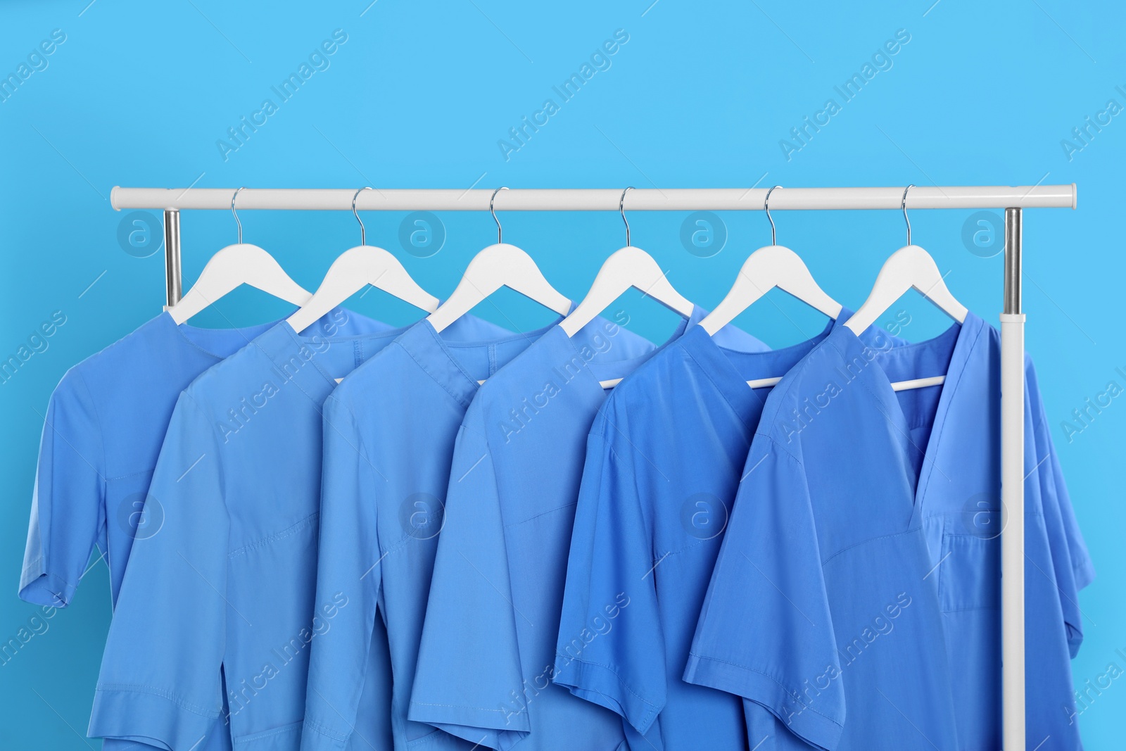 Photo of Medical uniforms on rack against light blue background