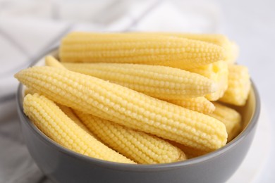 Tasty fresh yellow baby corns in bowl on white table, closeup