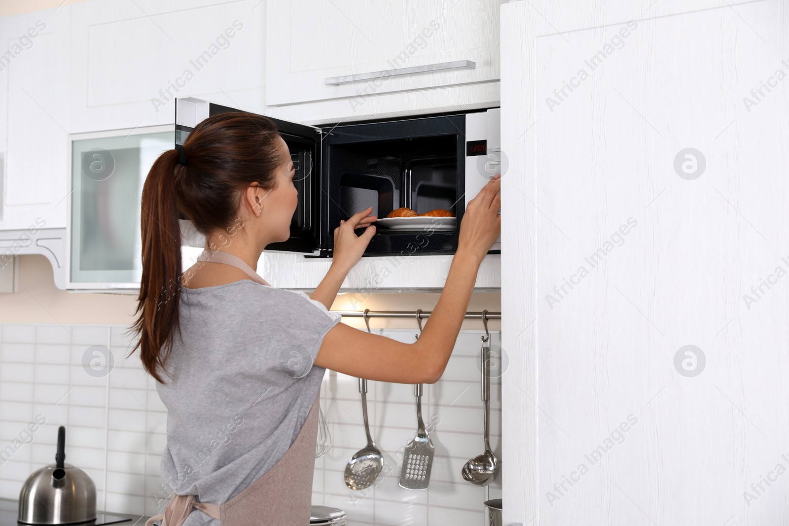 Photo of Young woman using microwave oven at home