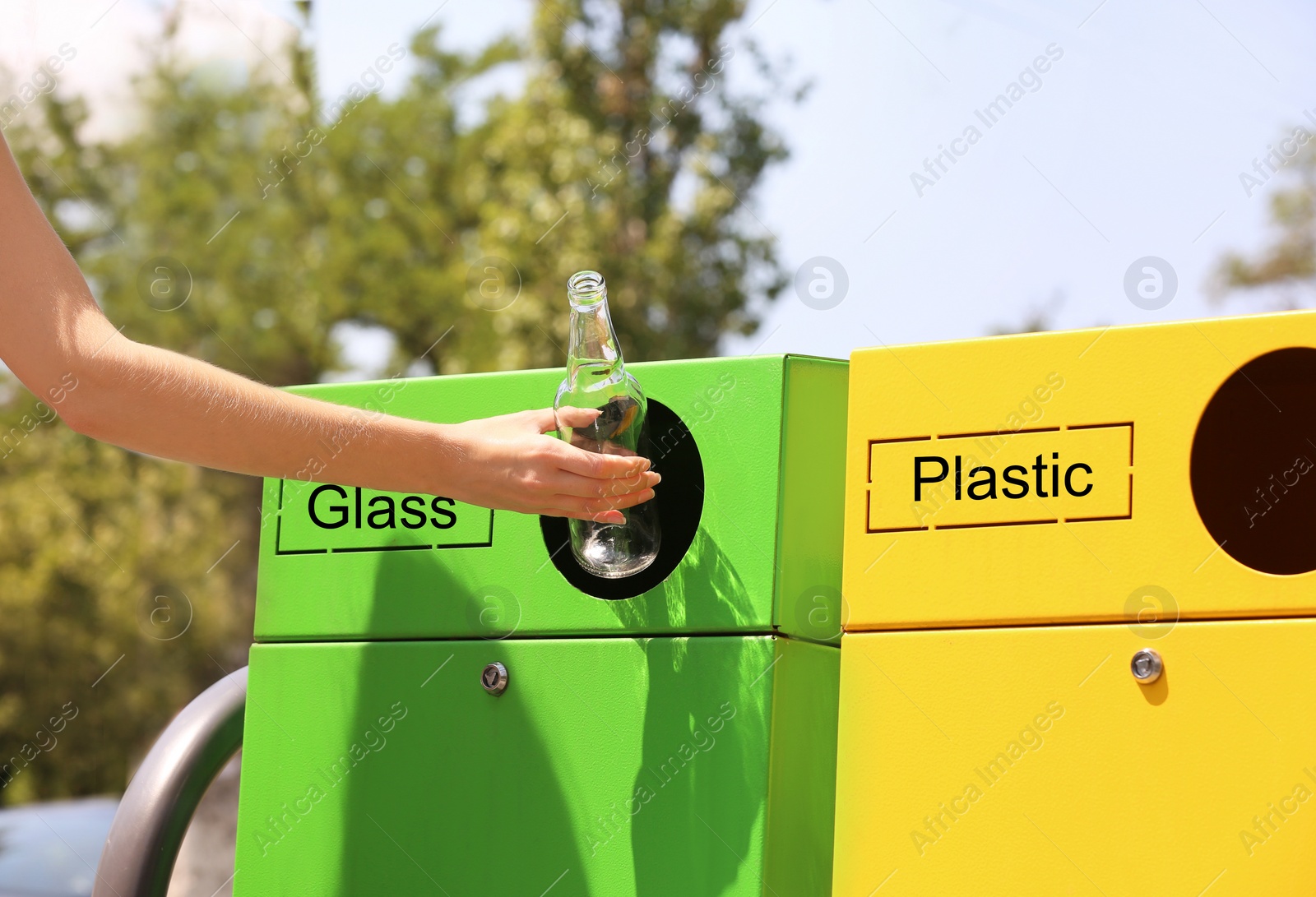 Photo of Woman throwing glass bottle into sorting bin on city street, closeup. Recycling waste