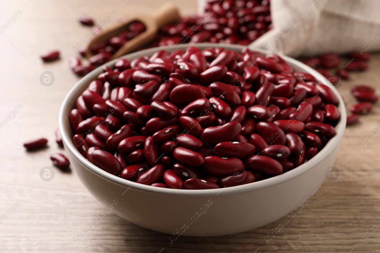 Photo of Raw red kidney beans in bowl on wooden table, closeup