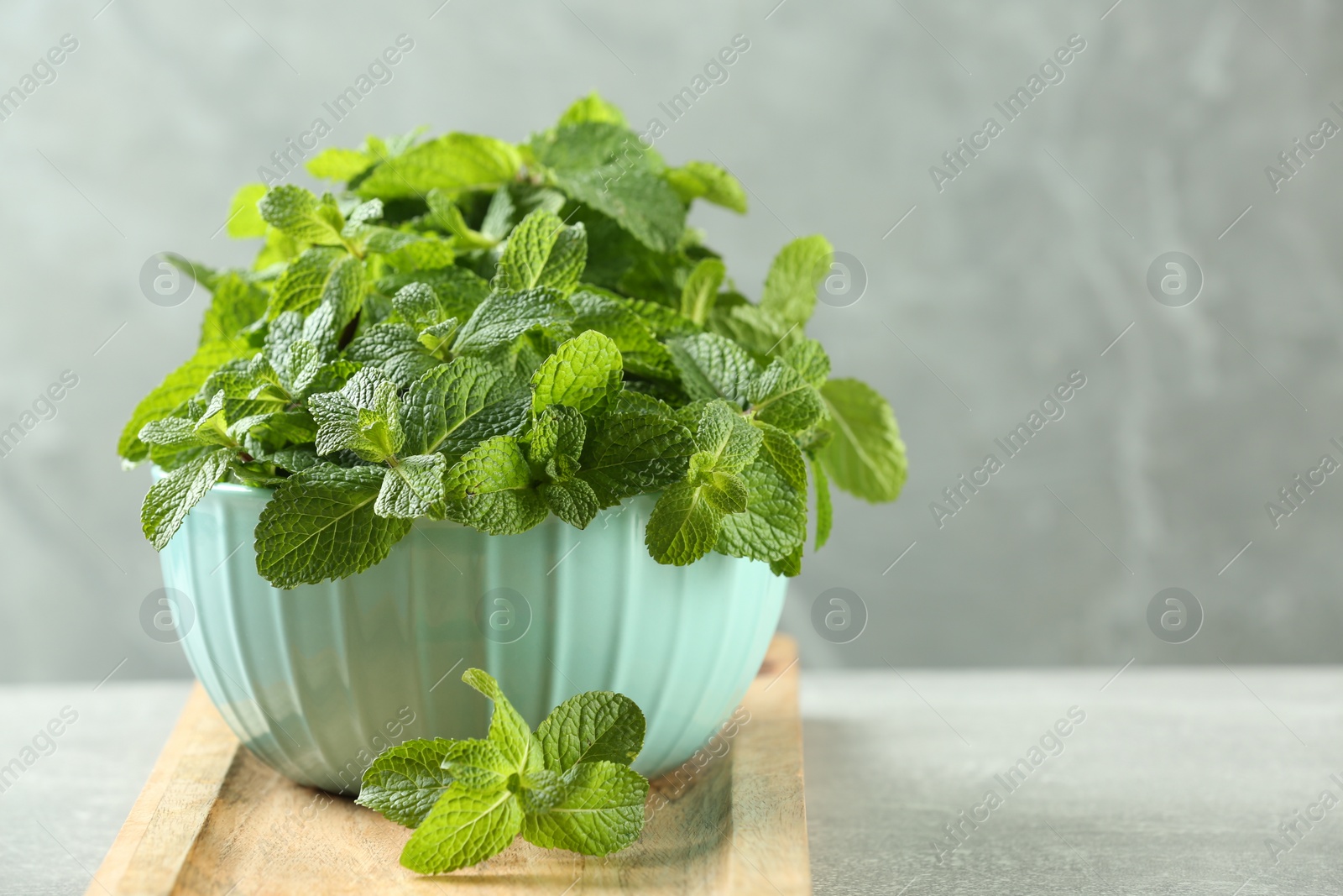 Photo of Bowl with fresh green mint leaves on grey table. Space for text