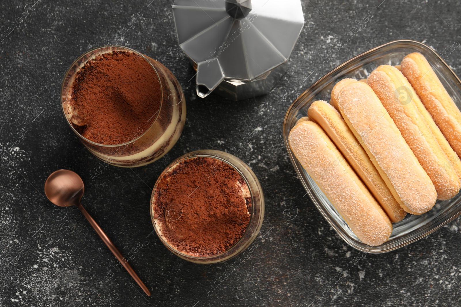 Photo of Delicious tiramisu in glasses and ingredients on grey textured table, flat lay