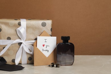 Photo of Happy Father's Day. Card with phrase I Love You, Daddy in envelope, cufflinks, perfume and gift box on light marble table, closeup. Space for text
