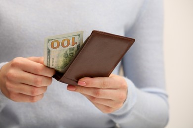 Photo of Woman holding brown leather wallet with 100 dollar bill on white background, closeup. Money exchange
