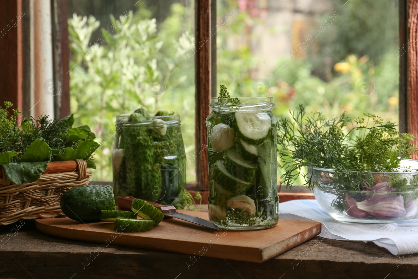 Photo of Glass jars, fresh cucumbers and herbs on wooden table indoors. Pickling recipe