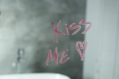 Photo of Red heart and phrase Kiss Me written with lipstick on mirror in bathroom, closeup