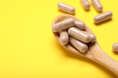 Photo of Gelatin capsules in spoon on yellow background, closeup. Space for text