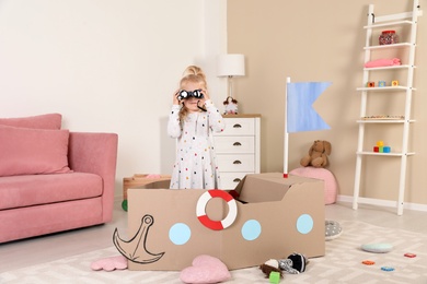 Cute little girl playing with cardboard ship at home