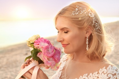 Photo of Happy bride holding wedding bouquet on beach
