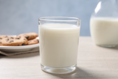 Glass of fresh milk near cookies on white table