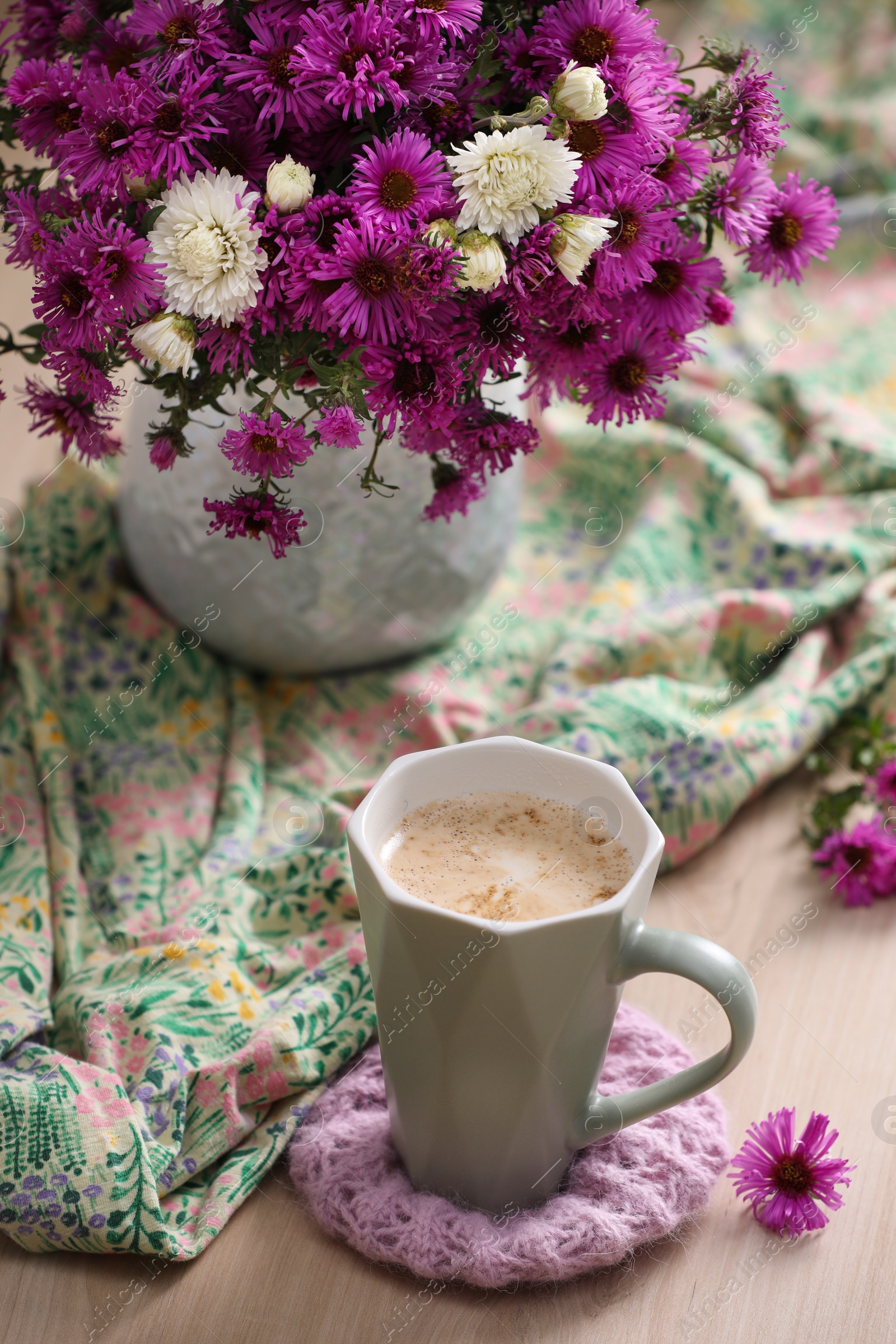 Photo of Cup of aromatic coffee, beautiful flowers and bright cloth on wooden table