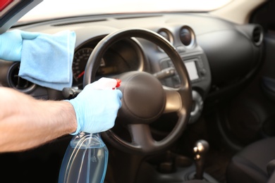 Photo of Man cleaning car salon with disinfectant spray and cloth, closeup