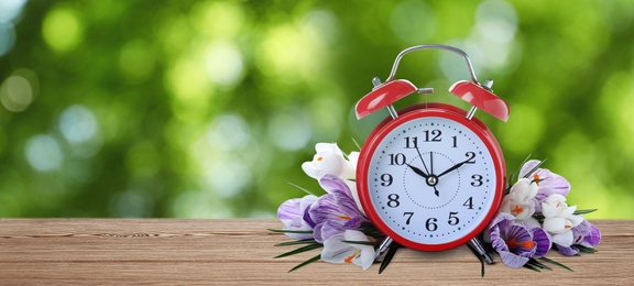 Image of Alarm clock and spring flowers on wooden table, space for text. Time change 