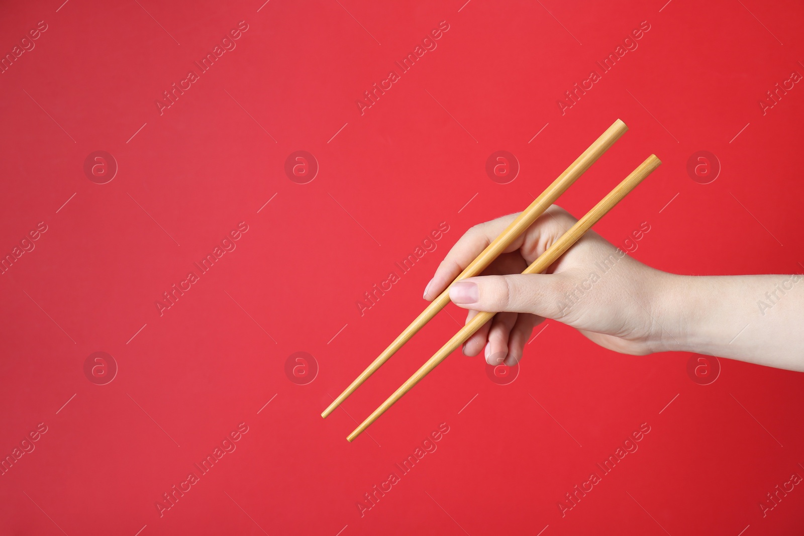 Photo of Woman holding pair of wooden chopsticks on red background, closeup. Space for text