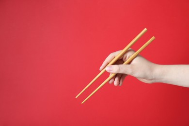 Photo of Woman holding pair of wooden chopsticks on red background, closeup. Space for text