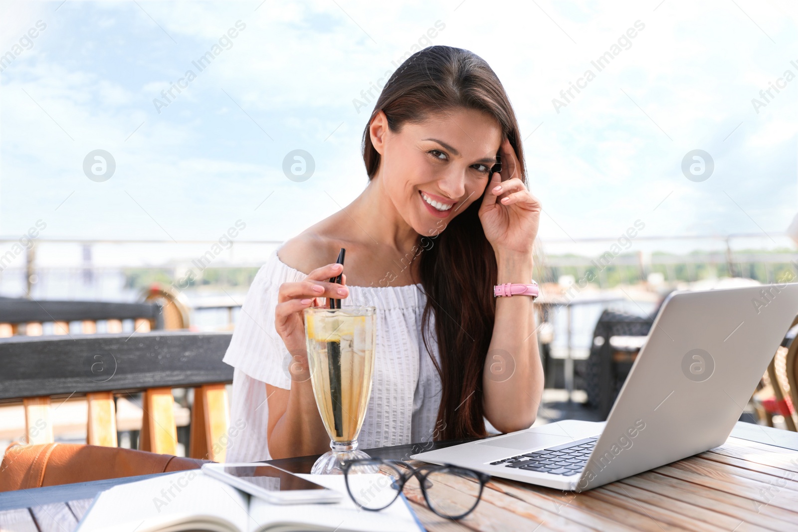 Photo of Beautiful woman with laptop and refreshing drink at outdoor cafe