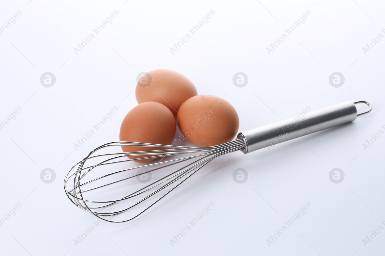 Photo of Metal whisk and raw eggs isolated on white