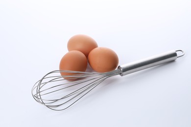 Photo of Metal whisk and raw eggs isolated on white