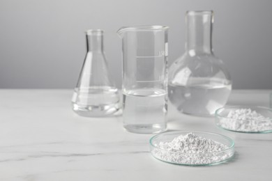 Photo of Petri dishes with calcium carbonate powder and laboratory glassware on white marble table. Space for text