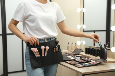 Photo of Professional makeup artist with belt organizer near wooden table indoors, closeup