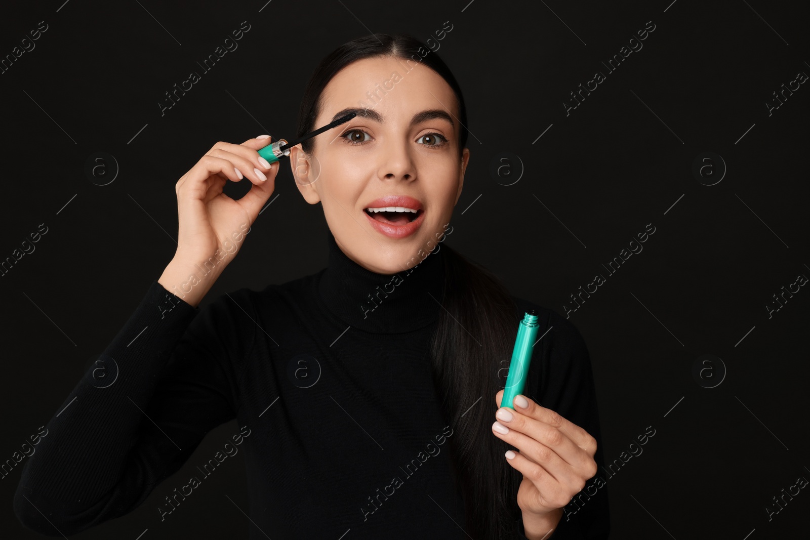 Photo of Beautiful young woman applying mascara on black background