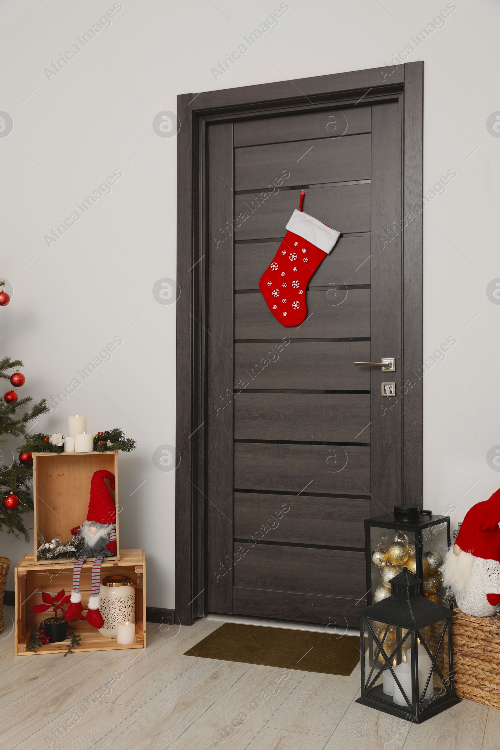 Photo of Christmas stocking hanging on wooden door and festive decoration indoors